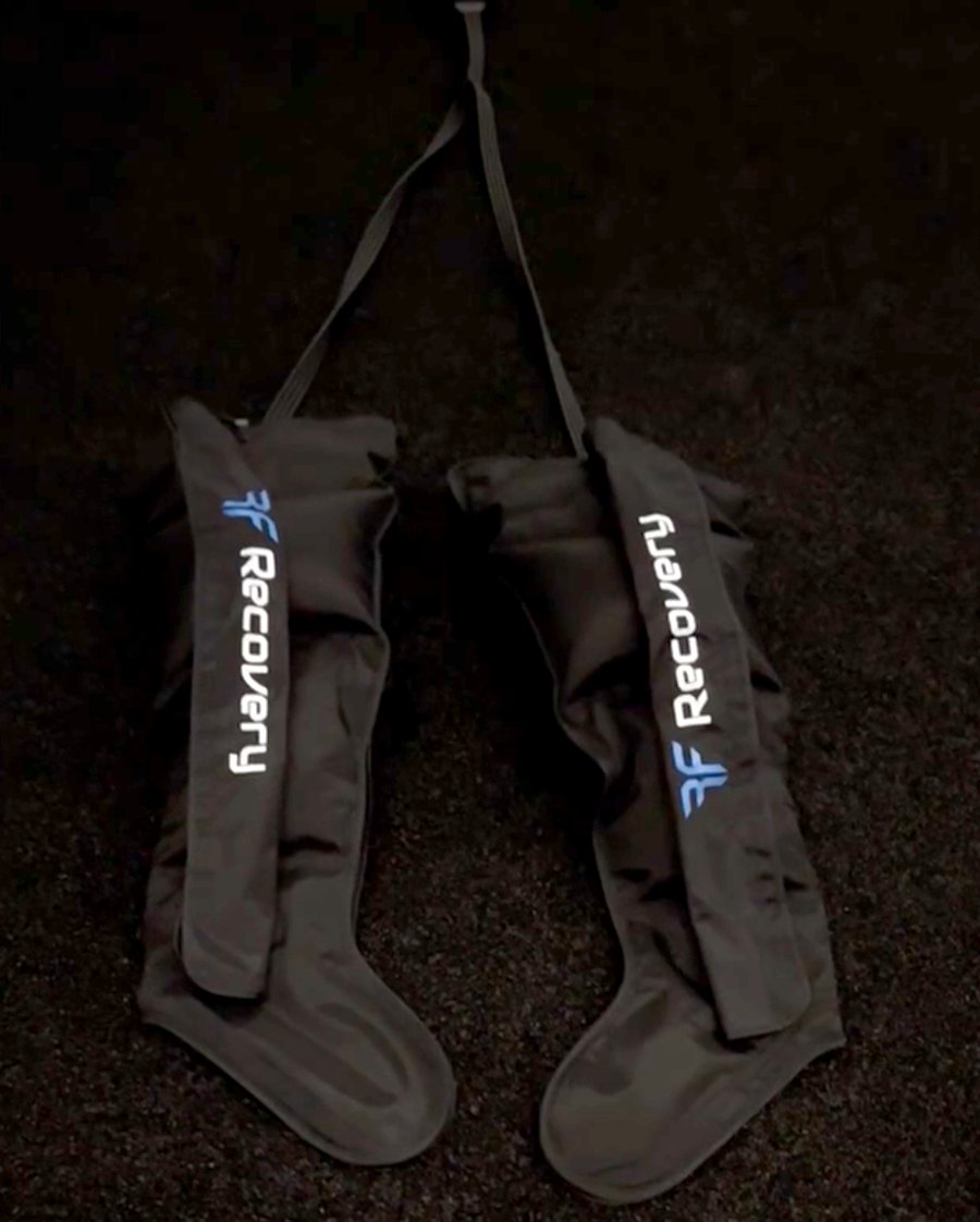 A pair of black compression recovery boots with straps, laid out on the floor
